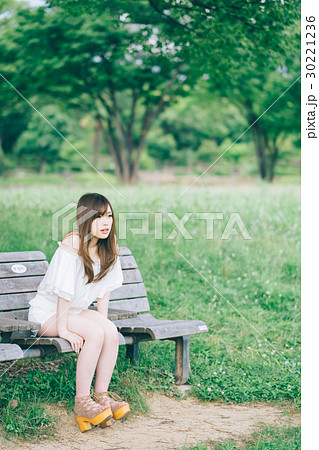 女性 公園 ベンチ 座るの写真素材