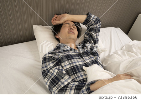寝起きに発熱がわかり、体調が悪くなって会社に行けないパジャマ姿の男性	
