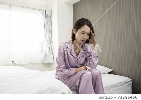 病気で寝込んでいる女性/体調の悪い女性/ベットに寝ている美しい女性/ベッドに座っている美人