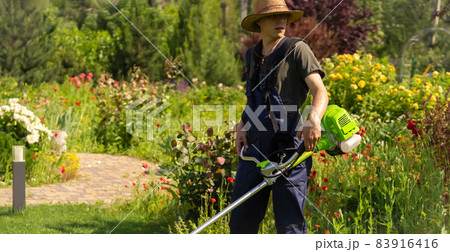 A Young White Man in a Straw Hat is Mowing a Lawn with a Lawn